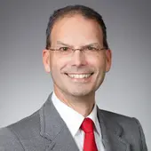 Dr. Stefan Insam, stv. Landesvorsitzender, im grauen Anzug mit roter Krawatte vor grauem Hintergrund