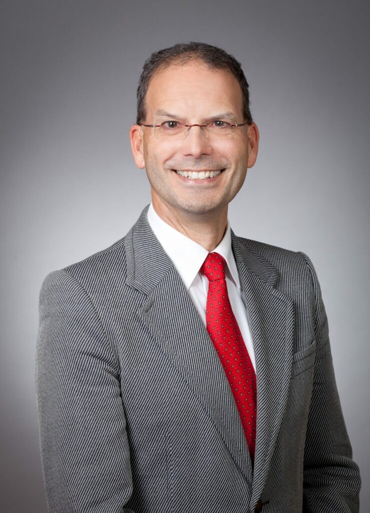 Dr. Stefan Insam, stellvertretender Landesvorsitzender des BBSB e. V., im grauen Anzug vor grauem Hintergrund.
